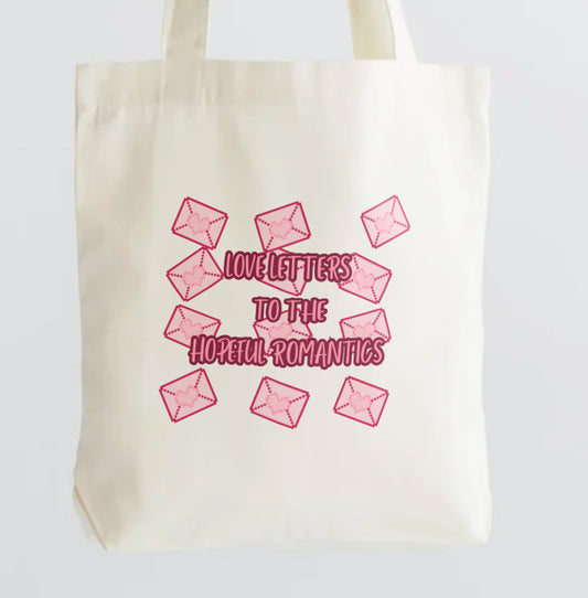Cream tote with pink envelopes and pink text that reads” love letters to the hopeful romantic” 